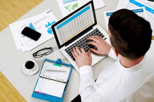 a man focused on his laptop, surrounded by papers and items, working on his personal financial statement