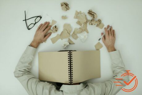 A man resting his head on a pile of crumpled paper, symbolizing the struggle of burnout and overwhelming stress.