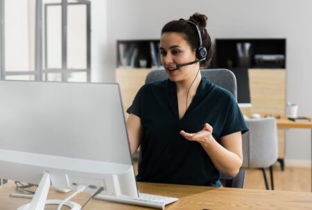 a woman in a headset sits at a desk with a computer, engaged in virtual assistant online training