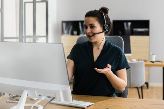 a woman in a headset sits at a desk with a computer, engaged in virtual assistant online training