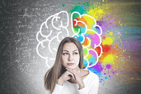 a woman examines a chalkboard displaying a brain, with a colorful rainbow backdrop, as part of her neuromarketing course