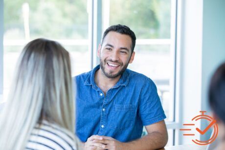 A man smiles warmly at a woman in an office, creating a supportive atmosphere for emotional clients.