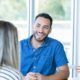 A man smiles warmly at a woman in an office, creating a supportive atmosphere for emotional clients.