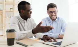 two men collaborate at a desk, focused on a laptop, discussing digital ads and strategies for effective marketing