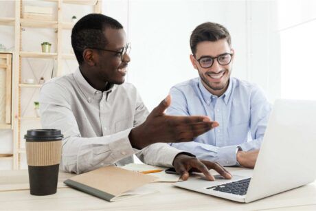 two men collaborate at a desk, focused on a laptop, discussing digital ads and strategies for effective marketing