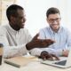 two men collaborate at a desk, focused on a laptop, discussing digital ads and strategies for effective marketing