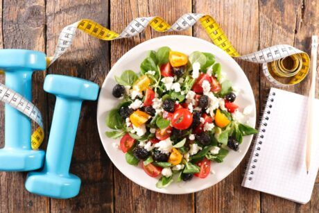 a nutritious salad displayed with blue dumbbells and a notebook, illustrating the concept of a healthy eating course