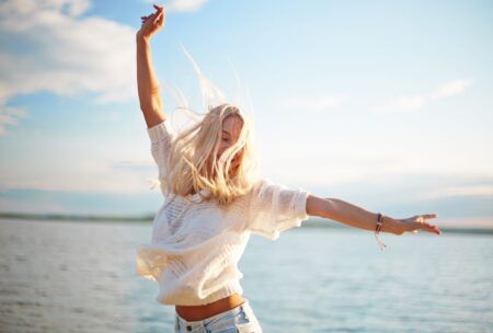 a woman in jeans and a white shirt gazes at the lake, reflecting on how to get superpowers​ for life and happiness