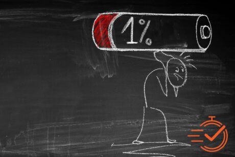 Chalk drawing of a stick figure carrying a large battery icon displaying 1% charge on a blackboard while overcoming burnout.