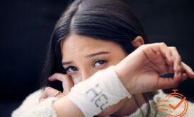 Person with long hair holds up her arm, revealing a white bandage with writing on it—a poignant reminder of struggles with self-harm and suicide thoughts.