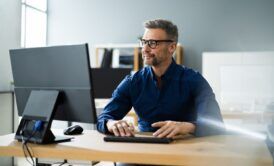 a man wearing glasses sits at a desk, focused on a computer during a wordpress masterclass session