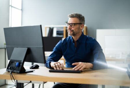 a man wearing glasses sits at a desk, focused on a computer during a wordpress masterclass session