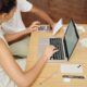 a man and woman discuss debt and credit while seated at a table with a laptop open between them