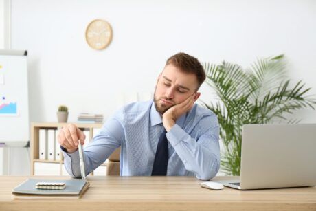 a man dressed in a shirt and tie works at a desk with a laptop, actively seeking strategies on how to overcome procrastination