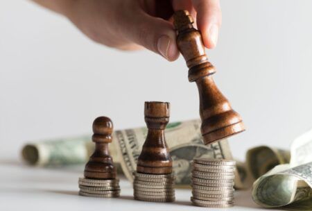 a person strategically places a wooden chess piece atop stacks of money, symbolizing thoughtful purchasing strategies