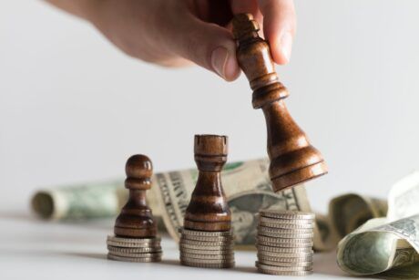 a person strategically places a wooden chess piece atop stacks of money, symbolizing thoughtful purchasing strategies