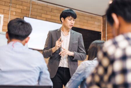 an asian man delivers a presentation to colleagues in a train the trainer course, fostering an interactive learning environment