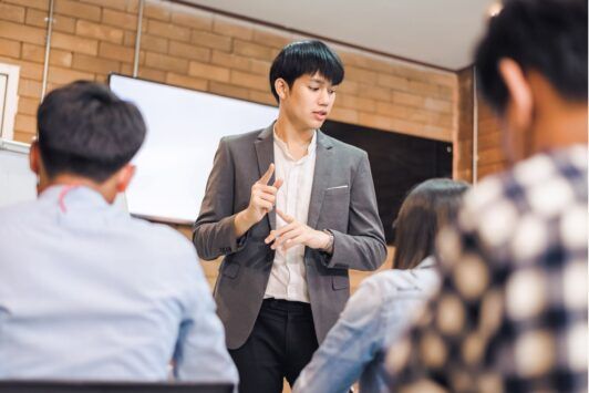 an asian man delivers a presentation to colleagues in a train the trainer course, fostering an interactive learning environment